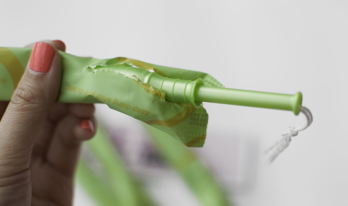 A hand holding a tampon with a plastic applicator.