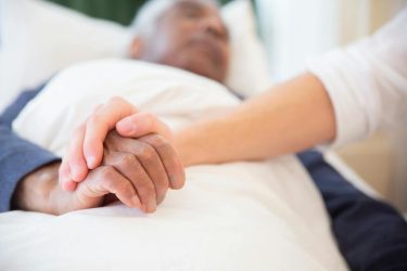 a young person holding an older person's hand lying in bed. palliative care