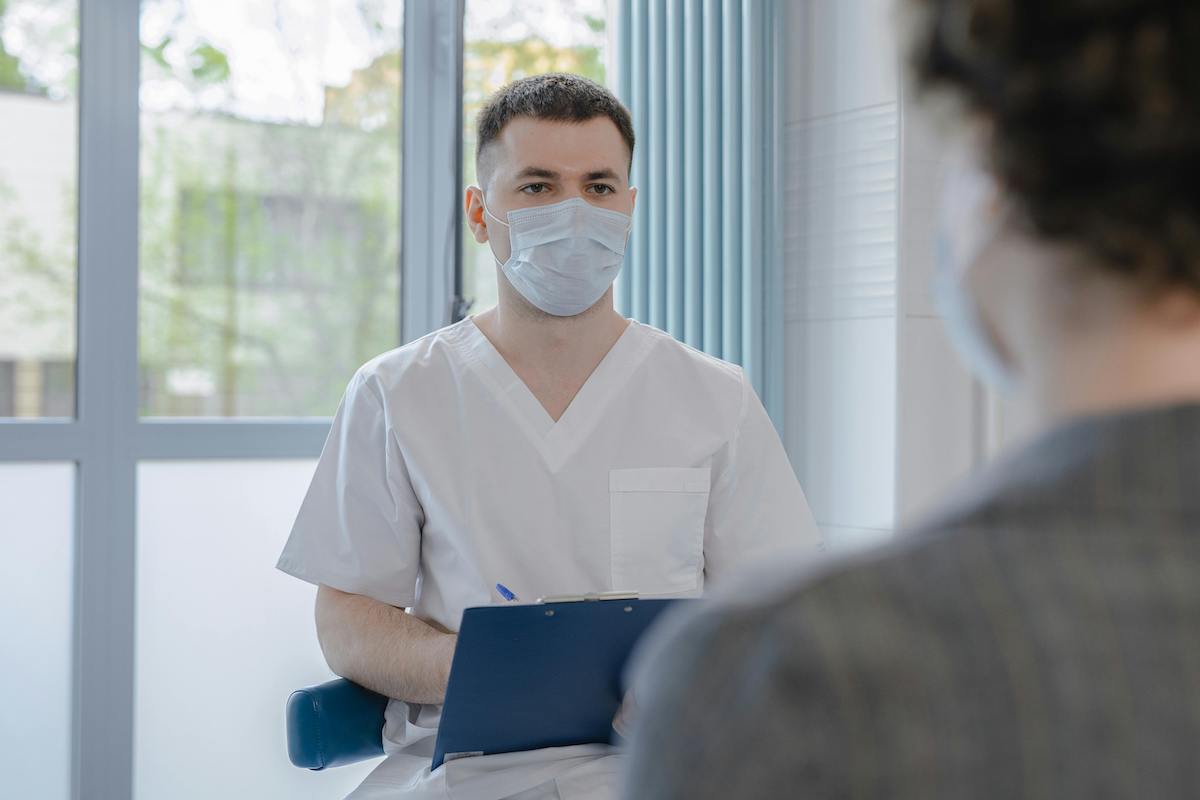 a doctor wearing a face mask talks to a patient