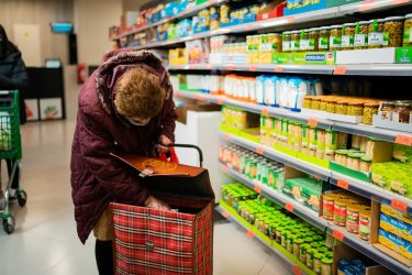 an older woman puts groceries in her bag at a supermarket. food security