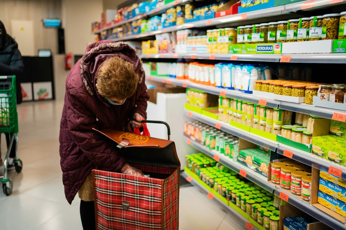 an older woman puts groceries in her bag at a supermarket. food security