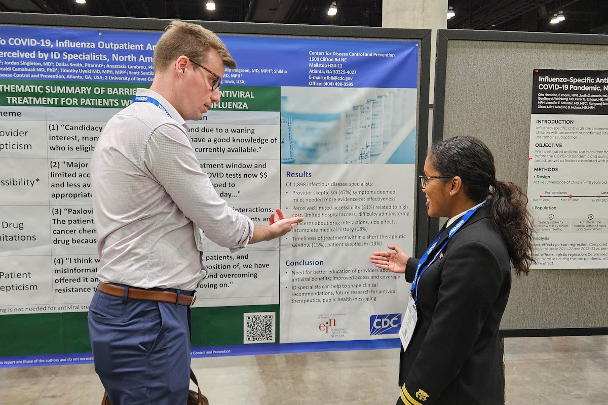 This image depicts Epidemic Intelligence Service (EIS) Officers, Class of 2023, Steven Langerman, MD (left) and Souci Louis, VMD (right), as they were discussing Officer Louis’ poster detailing barriers to COVID-19, and influenza outpatient antiviral treatment perceived by ID specialists, during the 2024 Los Angeles, California IDWeek meeting.