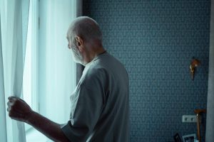 older adult man experiencing social isolation looks out a window