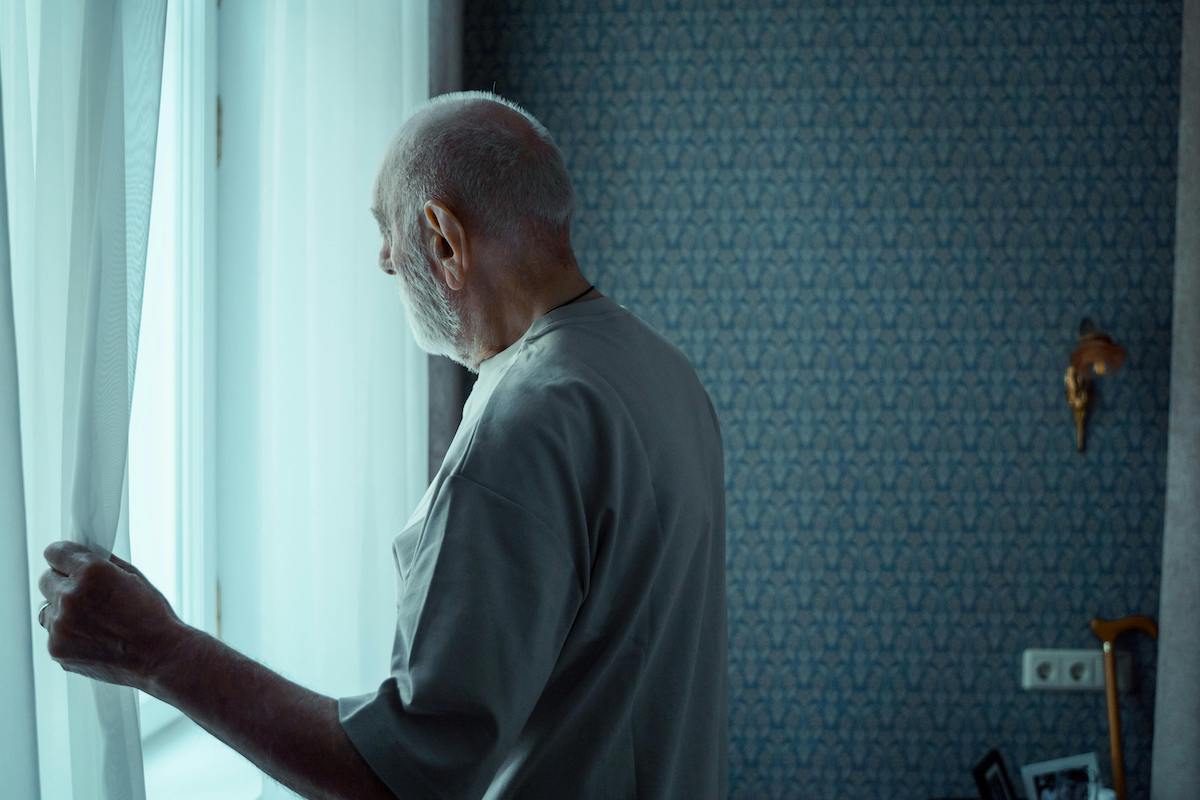older adult man experiencing social isolation looks out a window