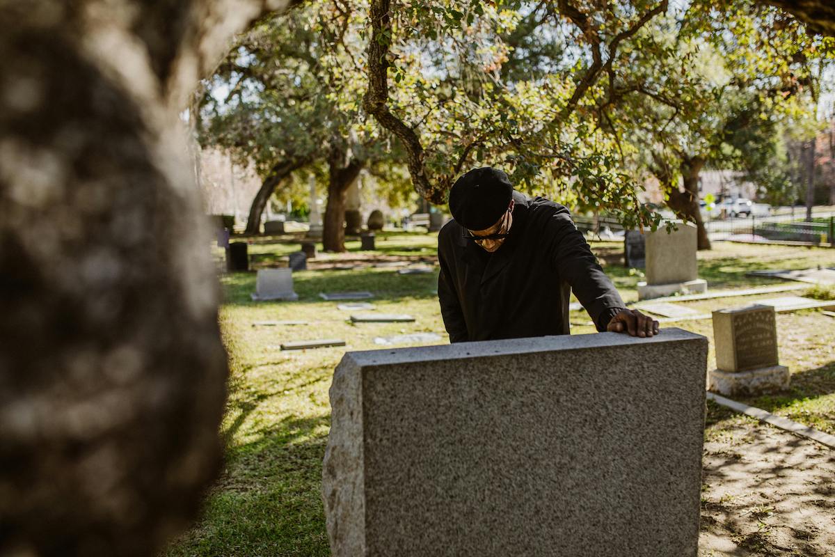 A Black man in a cemetery leaning over a tombstone