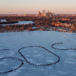 Hundreds of people form a human distress signal on Bde Maka Ska, a frozen lake in Minneapolis, with the city's skyline in the background.
