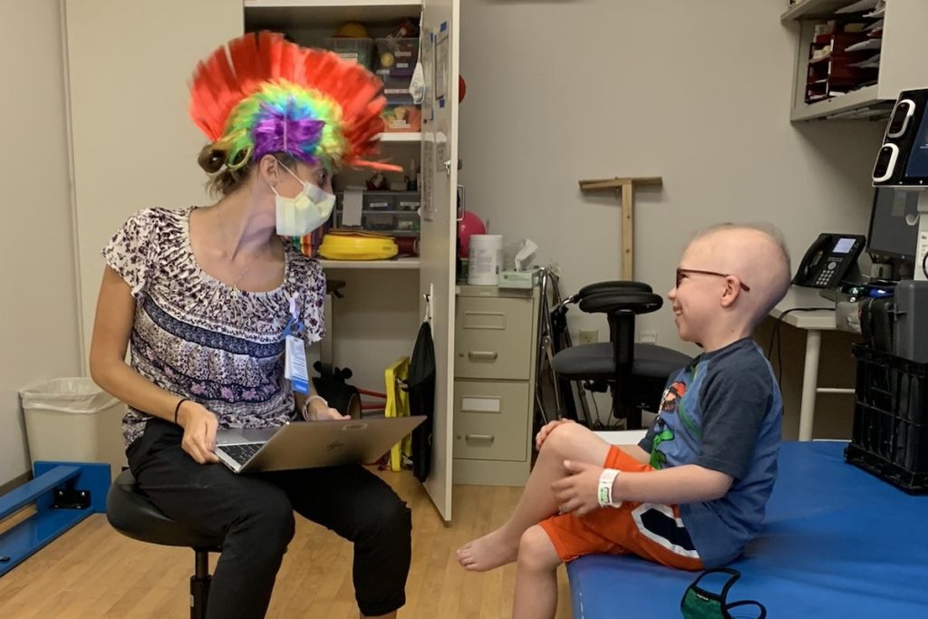a health care worker wearing a rainbow mohawk talks to a patient