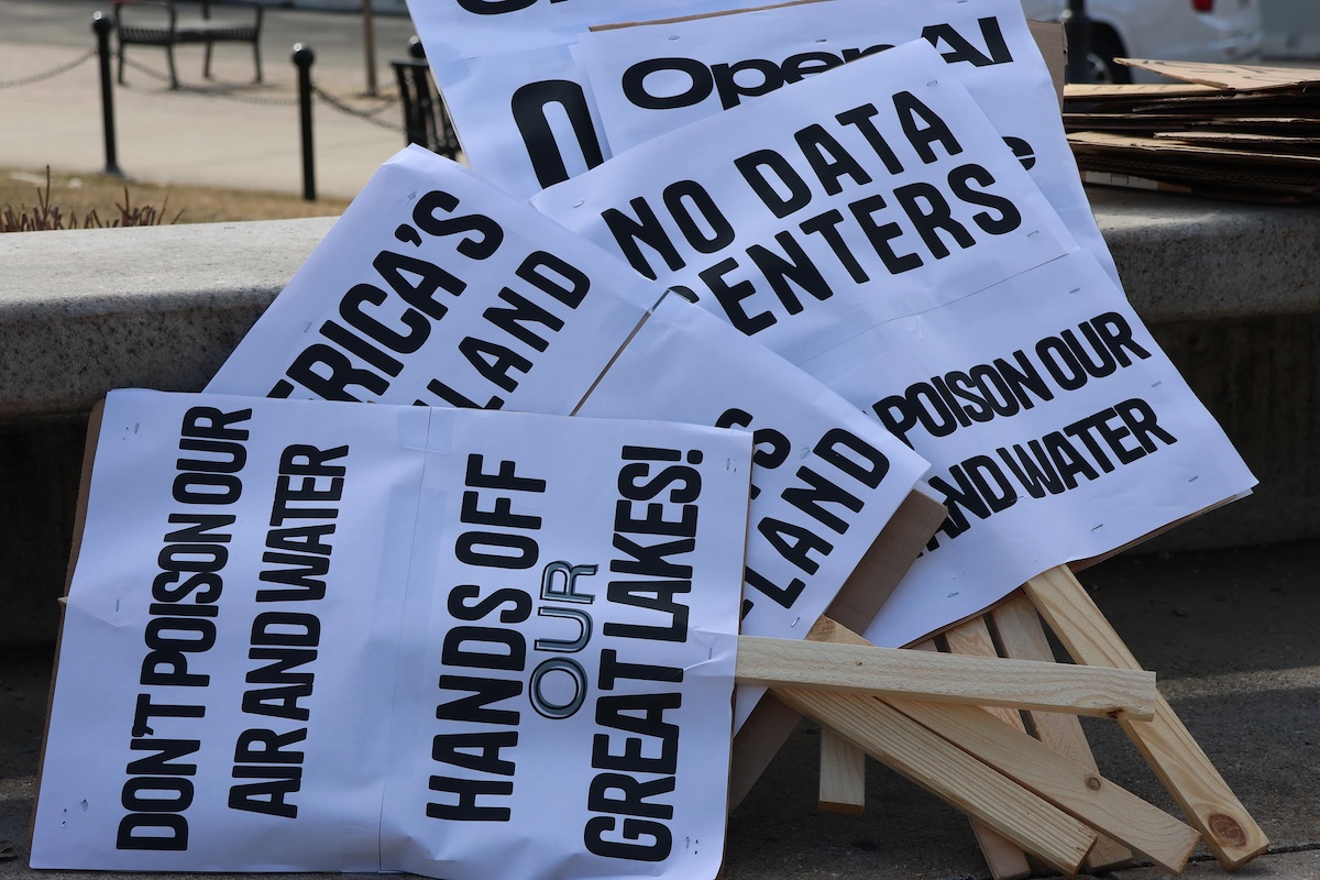 a collection of protest signs that read: "DON'T POISON OUR AIR AND WATER; HANDS OFF OUR GREAT LAKES!" "NO DATA CENTERS; DON'T POISON OUR AIR AND WATER" 