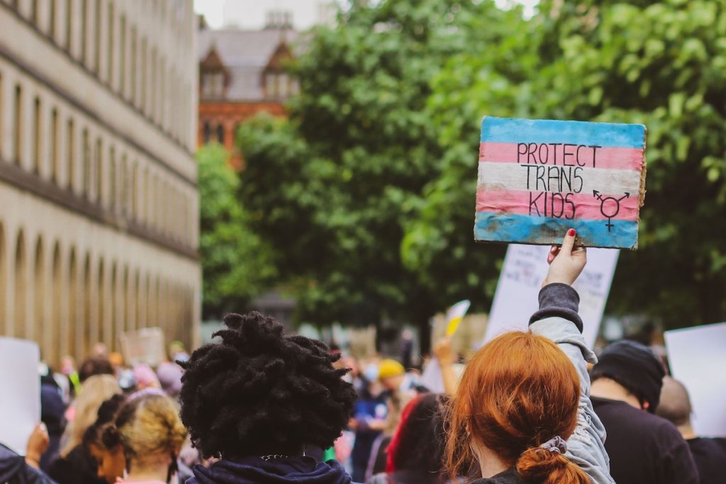 A protestor holds up a sign painted in a trans flag pattern that says "Protect Trans Kids"