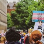 A protestor holds up a sign painted in a trans flag pattern that says "Protect Trans Kids"
