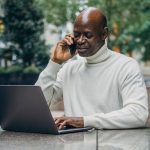 A Black man talking on a phone while on his laptop