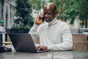 A Black man talking on a phone while on his laptop