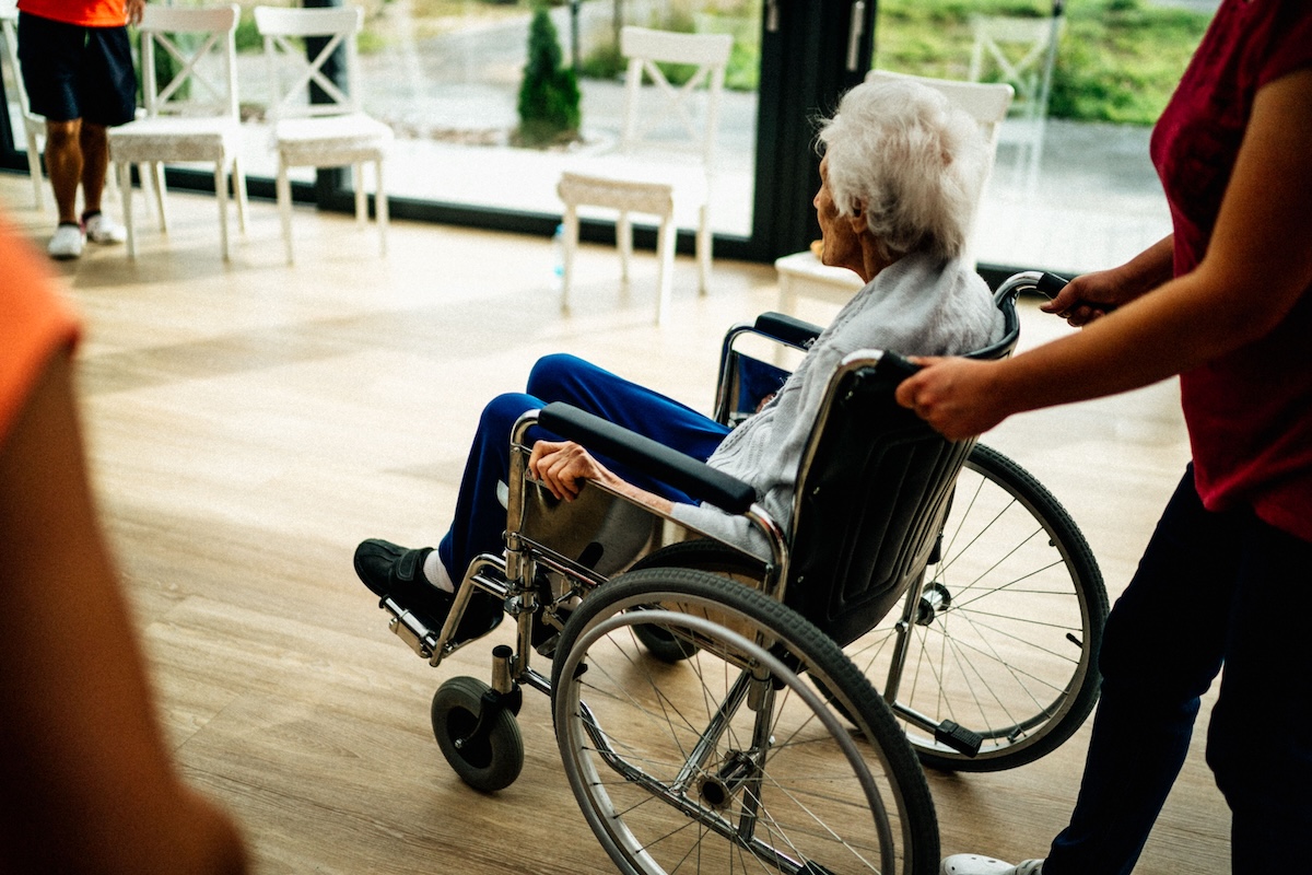an older adult in a wheelchair being pushed by a person in an end-of-life care facility