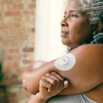 a woman wearing a continuous glucose remote patient monitoring device on her arm