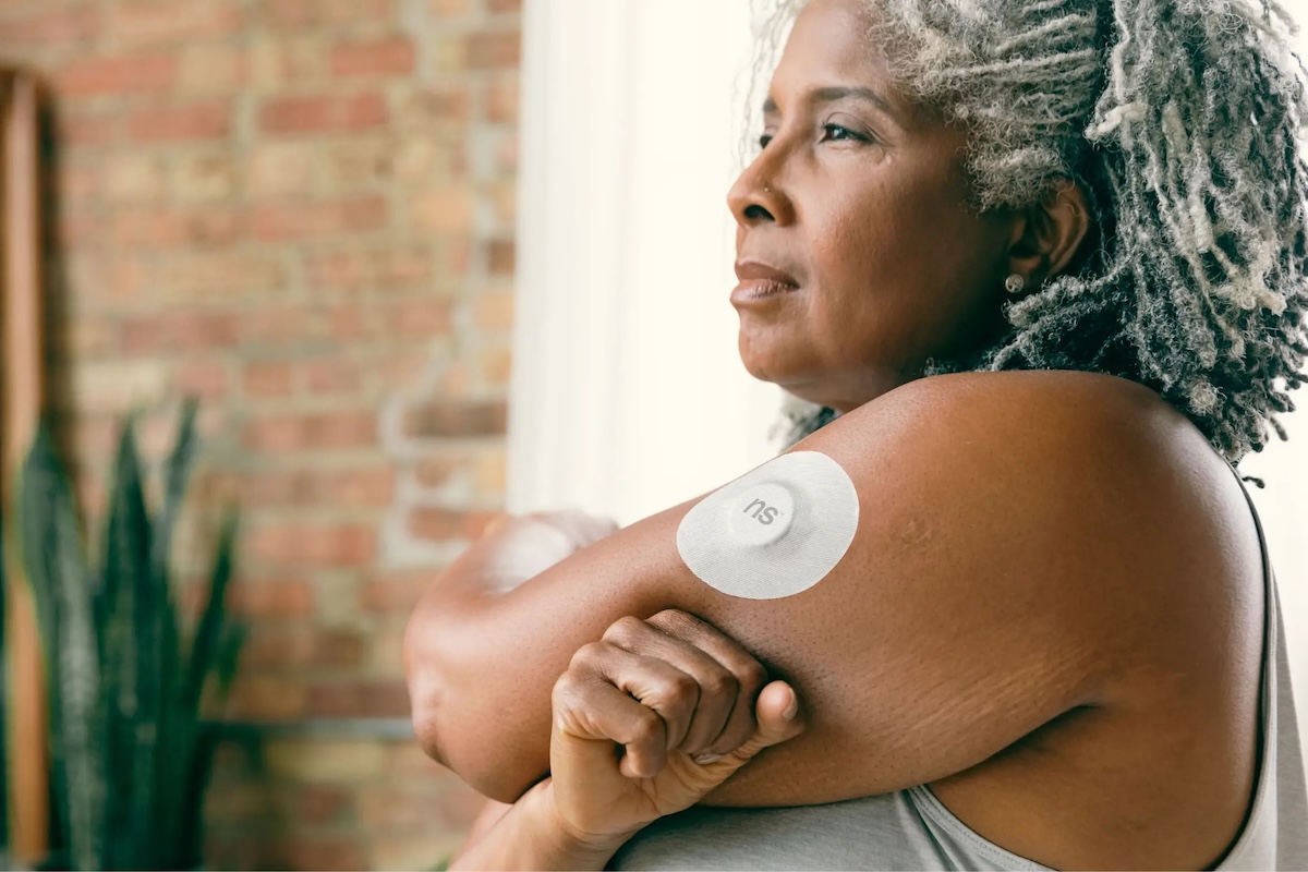 a woman wearing a continuous glucose remote patient monitoring device on her arm